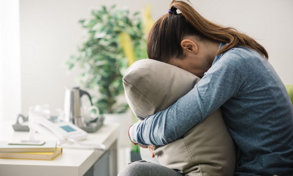 Unhappy lonely depressed woman at home, she is sitting on the couch and hiding her face on a pillow, depression concept; Shutterstock ID 504503110; Purchase Order: -